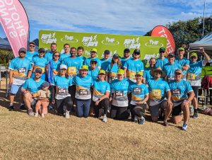 A large group of CleanCo staff, kneeling and standing in front of a media wall at the 2024 Ipswich Park2Park fun run event.