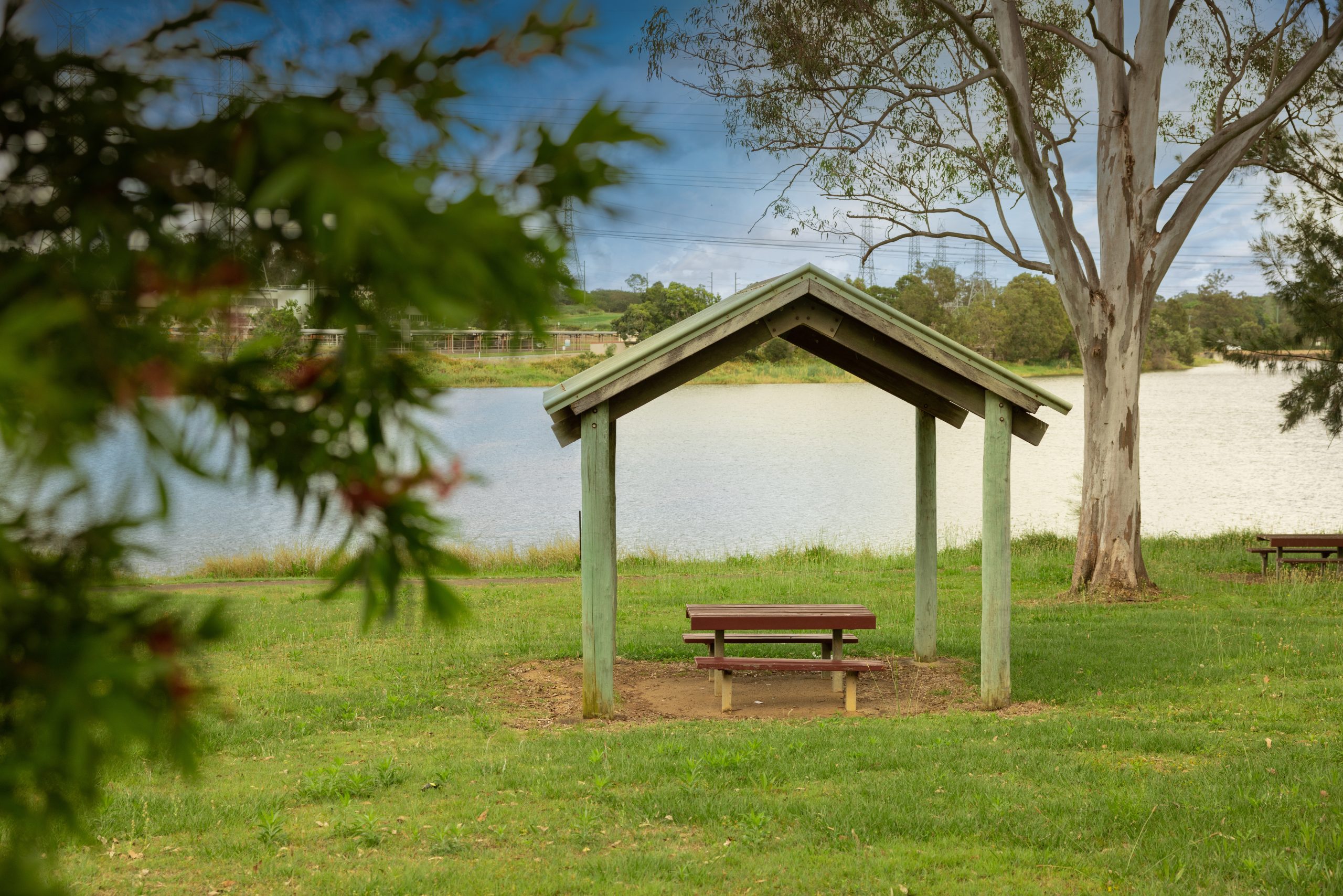 The Swanbank Visitors area. There are benches and trees in a beautiful green parkland next to the dam.