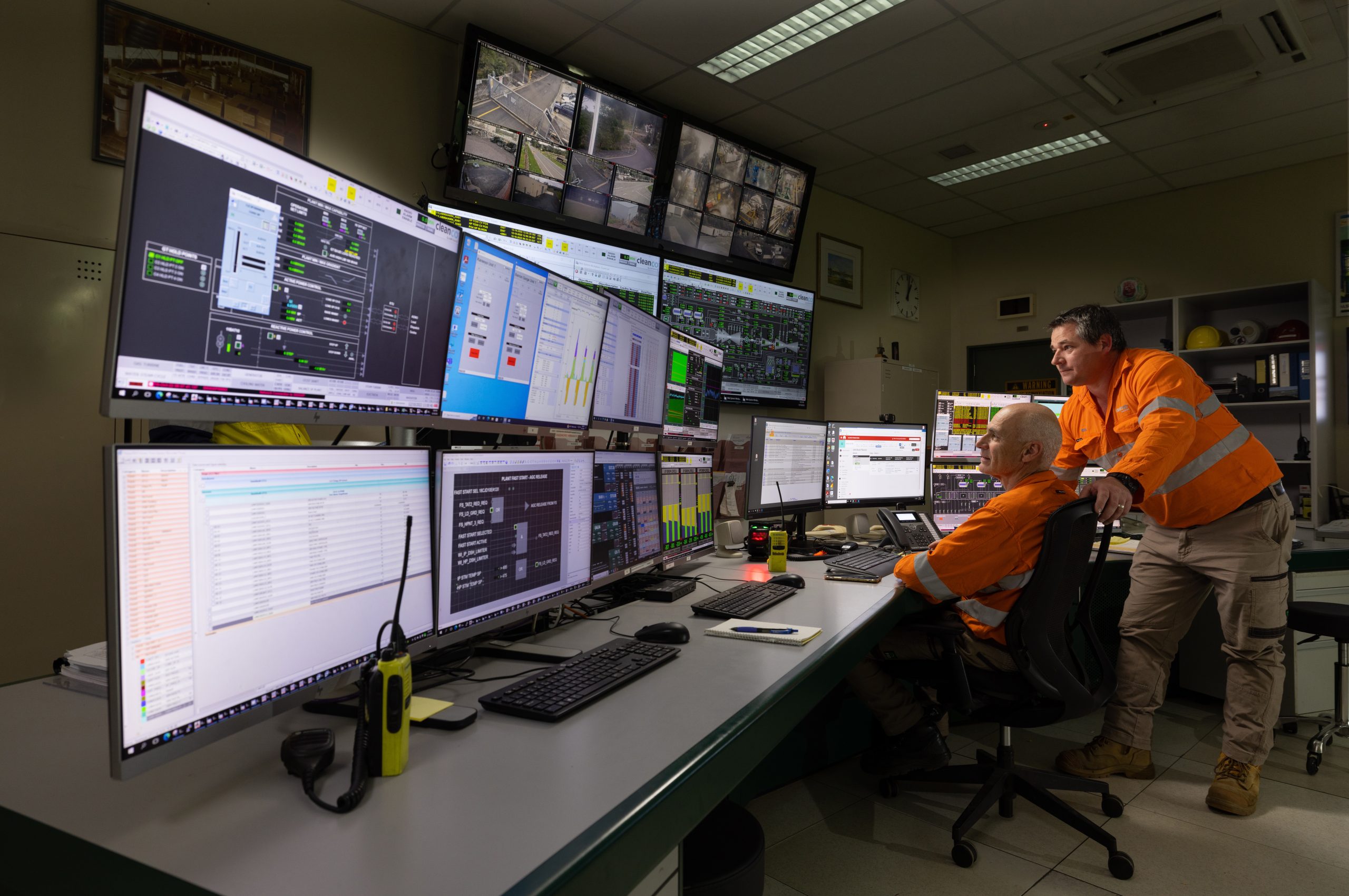 Two CleanCo workers at the Swanbank Power Station. They are wearing safety gear and staring at the many screens in the control room.