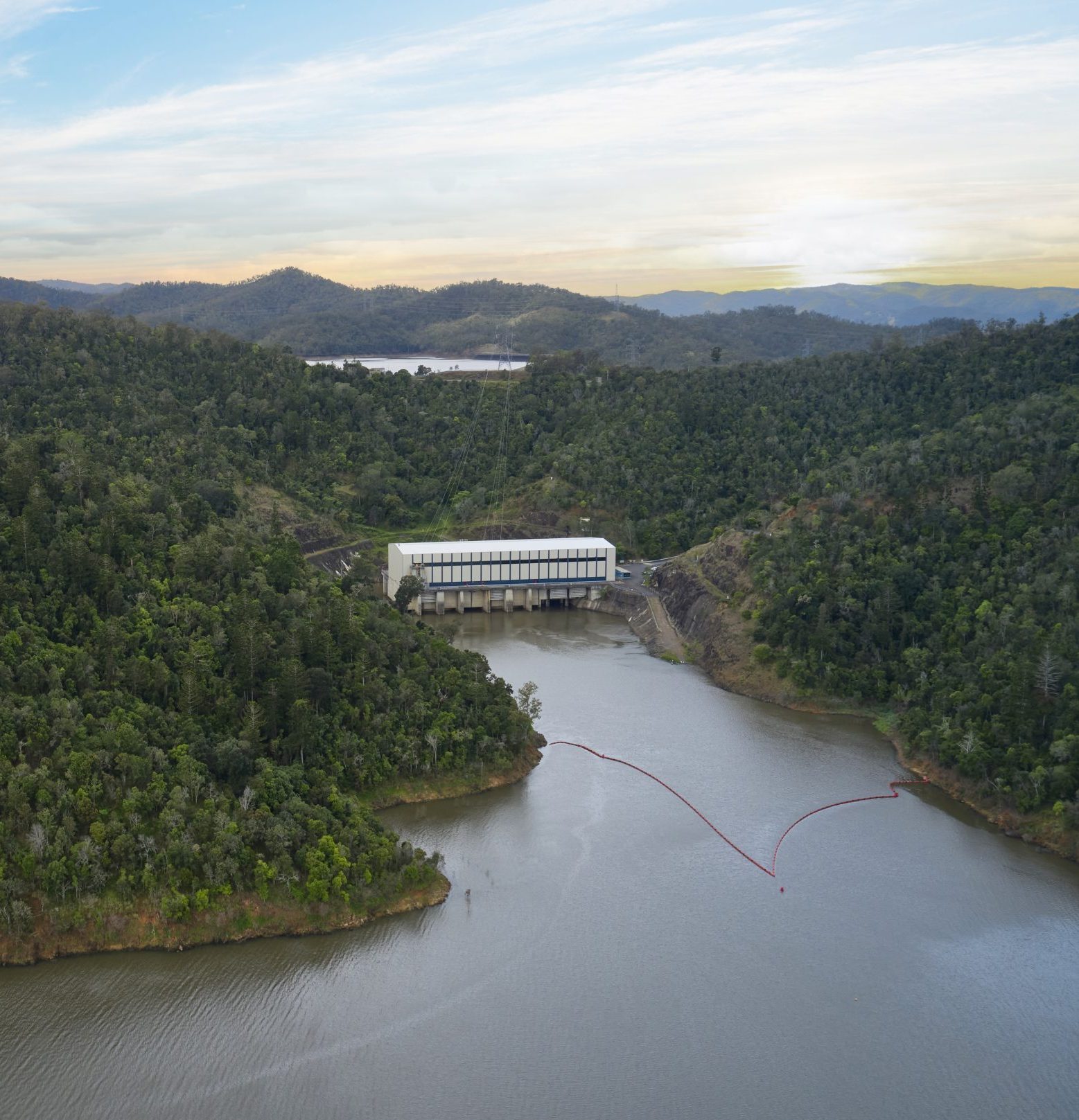 An aerial shot of the Wivenhoe Power Station. You can see green mountains and the sunrise as it appears over the dam.