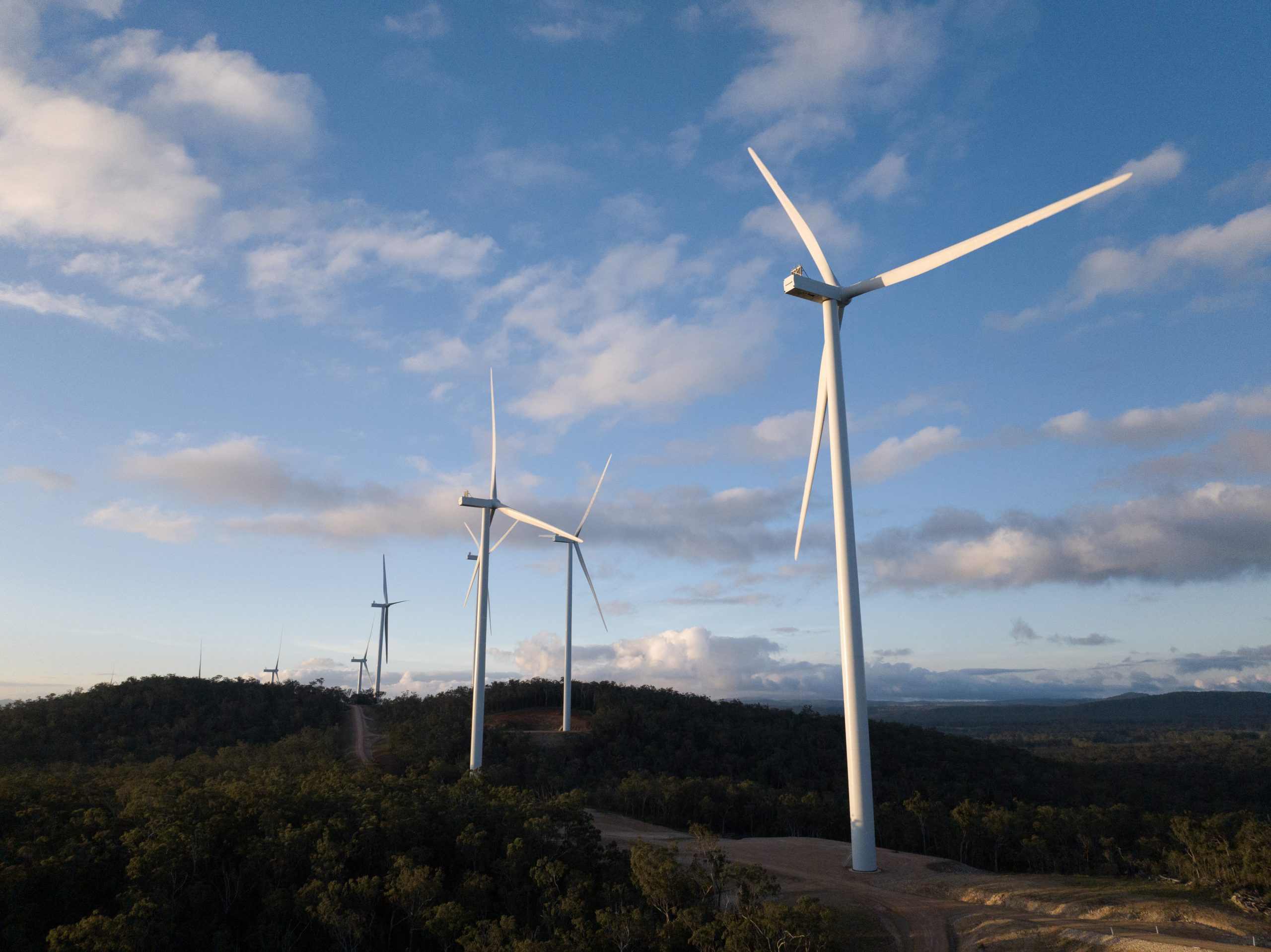 A panoramic shot of the wind turbines at the Kaban Green Power Hub. It has clear blue skies and white wind turbines dominating the skyline.