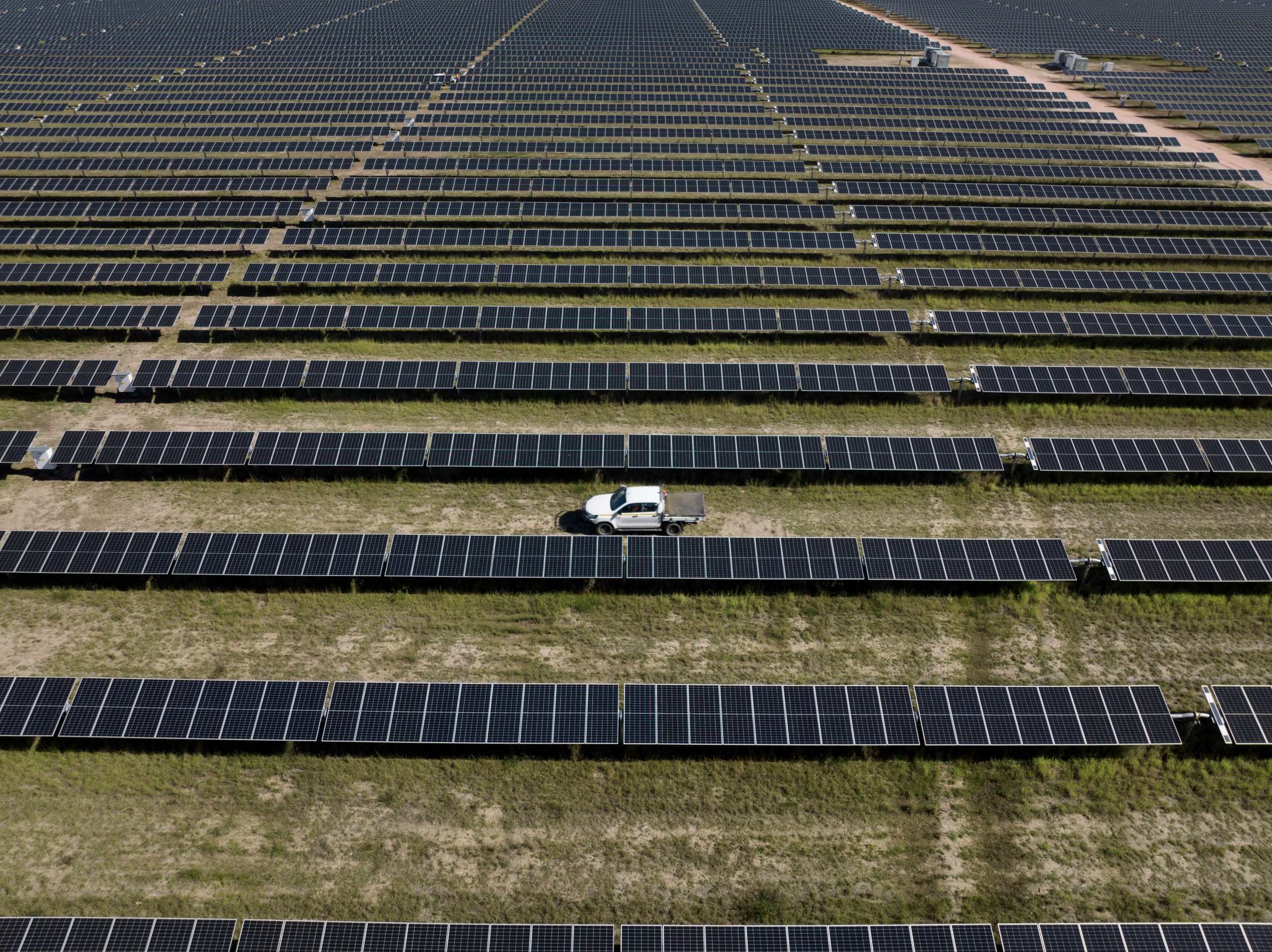 Aerial view of a ute driving through a row of solar panels