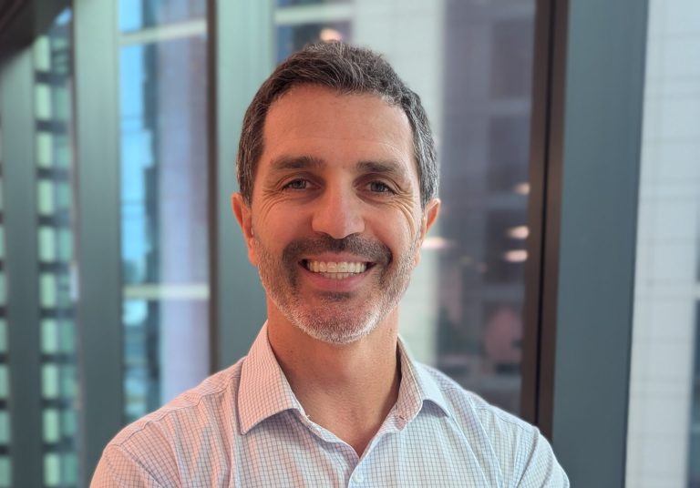 A CleanCo engineer sits on a table with his arms folded, smiling at the camera