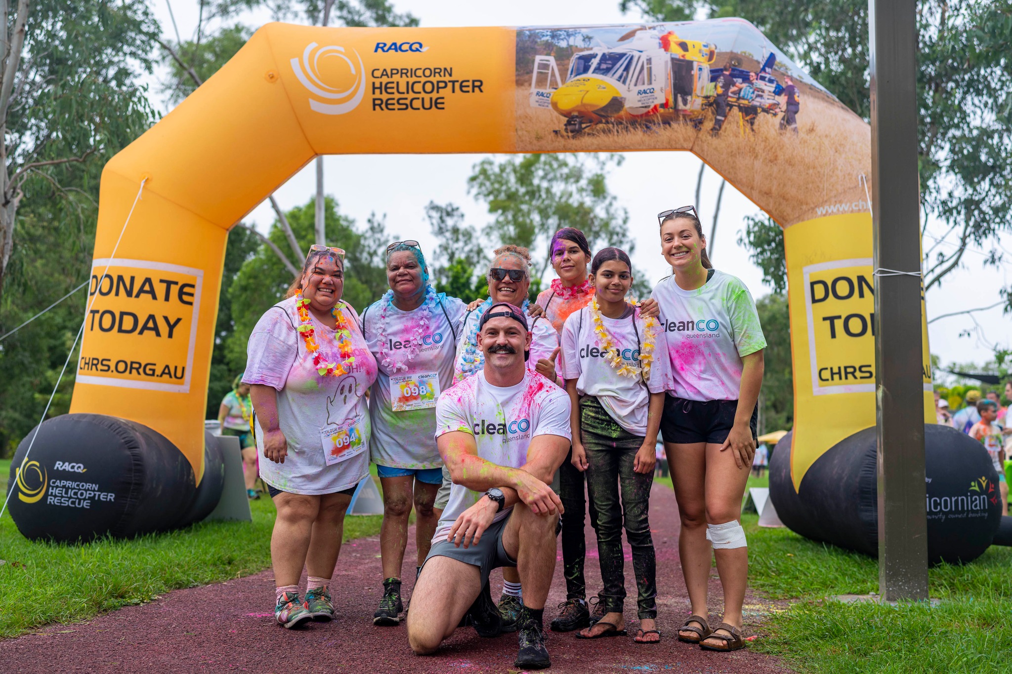 A group of women and a man stand beneath the finish line of the Colour Me Capciron colour fun run