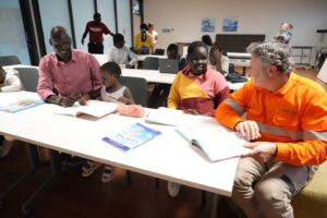 A CleanCo employee in high vis orange shirt sits at a desk with adults and young children who are participating in an after school homework club
